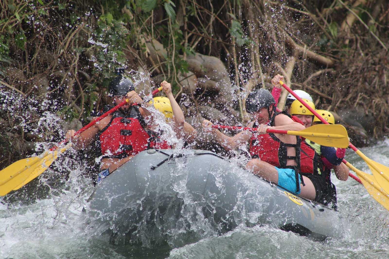 Group of people rafting on Class III rapids in the Sarapiqui River, Costa Rica, surrounded by tropical jungle during an adventure tour.